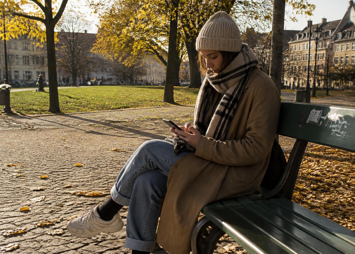 A person sitting on a park bench in autumn calmly planning on their phone