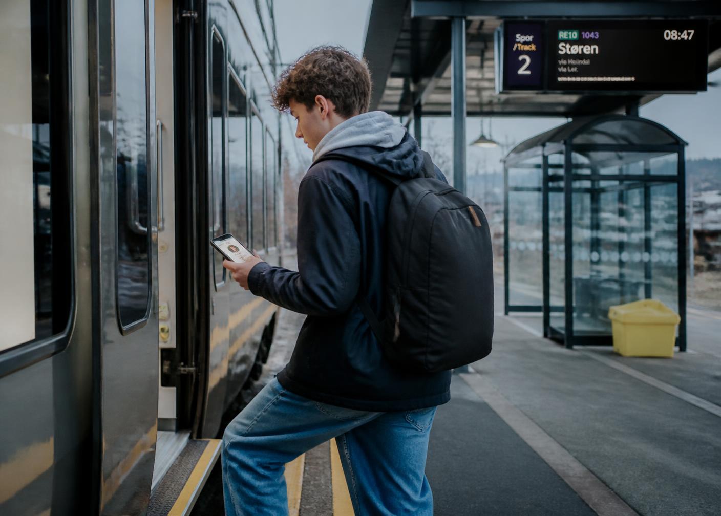 A teenager boarding a commuter train while sharing the trip from his phone